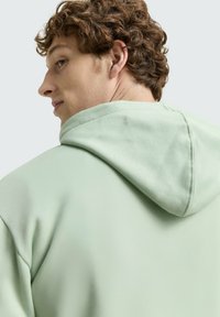 Felpa verde menta con cappuccio regolabile e tessuto morbido. La schiena presenta una texture liscia e cuciture pulite.