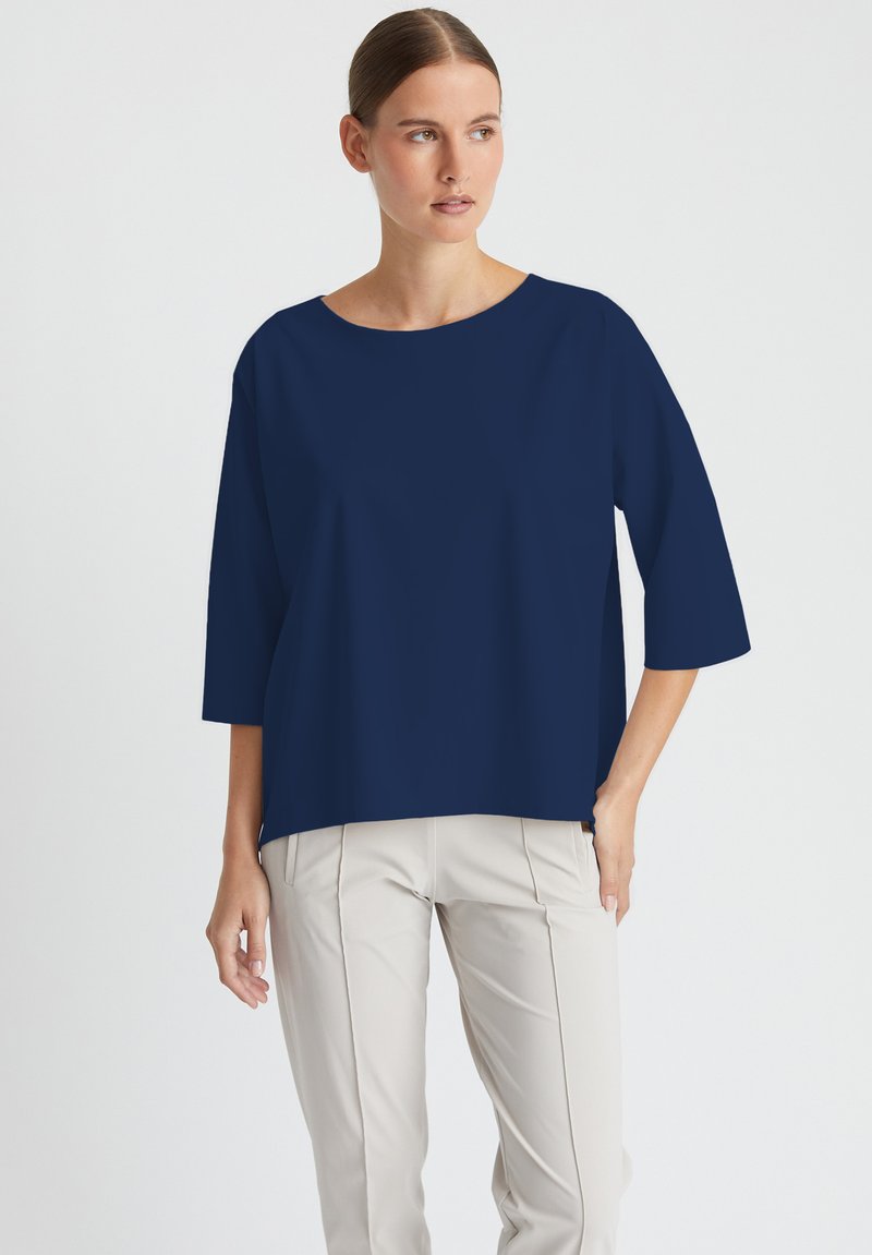 Marineblaues, übergroßes Blusenshirt mit Rundhalsausschnitt und drei Viertelärmeln. Leichter Stoff, kombiniert mit hellbeigen, taillierten Hosen.