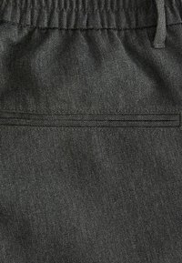 Tissu gris foncé avec une texture lisse, comportant une taille élastique et une poche arrière discrète avec un simple détail cousu.