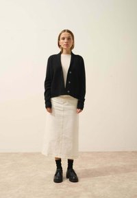 Czarny kardigan z guzikami, kremowy sweter, biały dżinsowy spódniczka i czarne buty. Prosty design, teksturowane tkaniny i neutralne kolory.