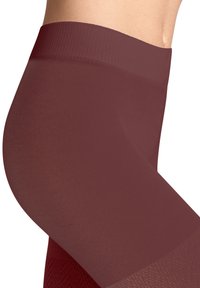 Zbliżenie osoby noszącej bezszwowe bordo legginsy kompresyjne, ukazujące wysoki pas i teksturowany materiał.