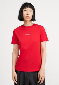 Red cotton T-shirt with short sleeves, crew neck, and "Calvin Klein Jeans" text in white across the chest. Plain design with no patterns.