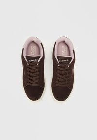 Brown suede sneakers with a white rubber sole, round toe, and dark brown laces. Soft pink lining and branding on the insole.