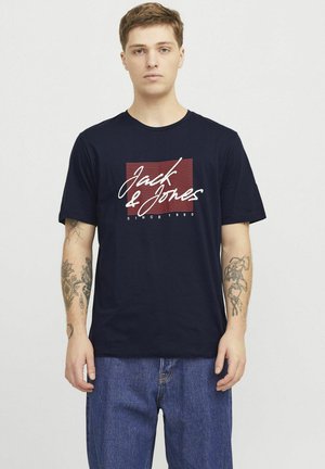 Granatowa bawełniana koszulka z białym napisem "Jack & Jones", czerwonymi poziomymi paskami oraz okrągłym dekoltem. Noszona z dżinsami.