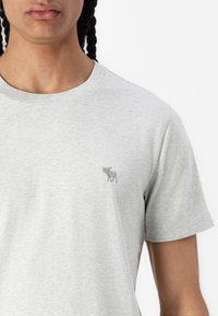 Grå kortærmet t-shirt med rund halsudskæring. Har et lille, grå broderet moose-logo på venstre bryst. Blødt, tekstureret stof.