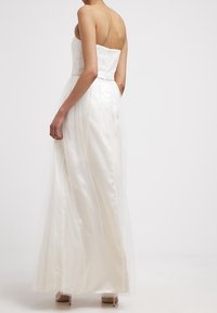 Abito bianco senza spalline con un corpetto di pizzo e una gonna in tulle. Presenta una vita aderente e un orlo fluente, completato da una finitura in satin morbido.
