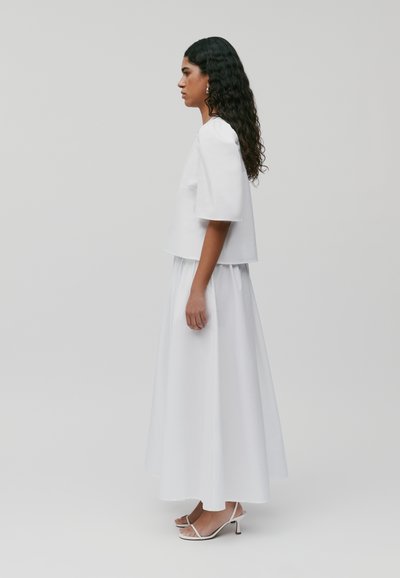 Witte kortemouwen top en vloeiende enkellange rok, beide in een soepele stof. Gemaakt met witte haksandalen en minimalistische zilveren oorbellen.