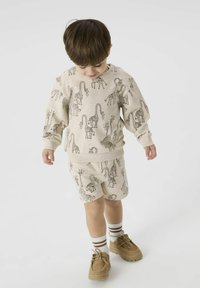 Sweatshirt beige à manches courtes et shorts avec des motifs de girafe noirs, associés à des chaussures beiges et des chaussettes blanches avec des rayures marron.