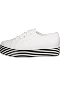 White canvas sneaker with a rounded toe, lace-up design, and a thick black-and-white striped platform sole. Textured upper material.