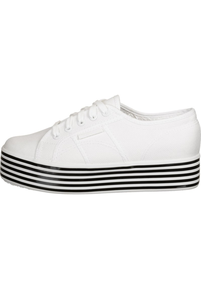 White canvas sneaker with a rounded toe, lace-up design, and a thick black-and-white striped platform sole. Textured upper material.