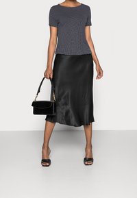 Marinblå topp med pricka mönster och kort ärm, kombinerad med en svart satin midi kjol, tillsammans med en svart handväska med guldkedja detaljer.