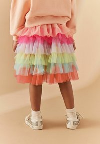 Jupe en tulle multicolore avec des couches de rose, de vert et d'orange, associée à des baskets argentées pailletées et des chaussettes blanches côtelées.