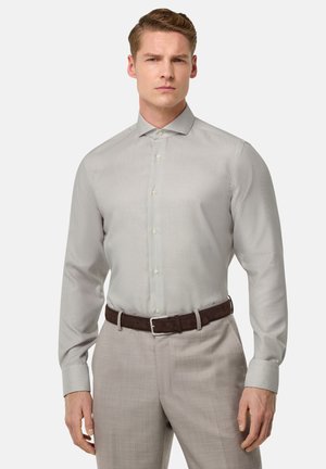 Camisa de vestir gris claro con un sutil patrón texturizado, cierre de botones en la parte frontal y cuello extendido, combinada con pantalones claros y un cinturón marrón.