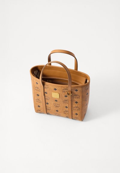 Tan leather MCM tote bag with double handles, zippered inner pocket, and black logo pattern on the exterior.