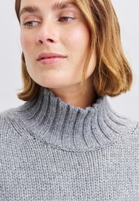 Hellgrauer Strickpullover mit rippenförmigem Rollkragen. Verfügt über grobe Nähte und eine weiche Textur, die das warme, gemütliche Design unterstreicht.