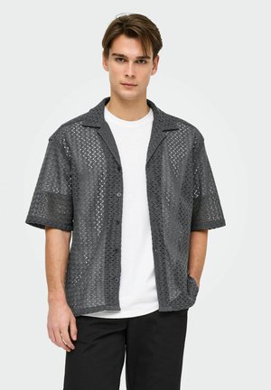 Gray short-sleeve shirt with a triangular mesh pattern, button closure, and a notched collar, worn over a white t-shirt.