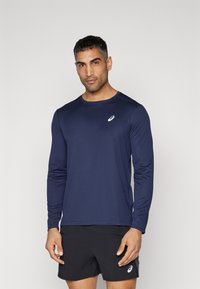 Langærmet atletisk skjorte i mørkeblå stof med rund halsudskæring og hvidt logo. Kombineret med sorte shorts, som viser en behagelig pasform.