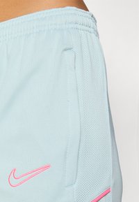 Light blue shorts with a breathable mesh texture and a pink embroidered logo. Features side pockets and an elastic waistband.