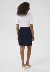 Haut blanc ajusté à manches courtes associé à une jupe élastique bleu marine. La jupe tombe au-dessus des genoux, avec une texture lisse et un design simple.