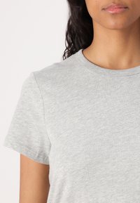 Tricou din bumbac gri, cu guler rotund și mâneci scurte, având o textură moale și un model ușor melanj.