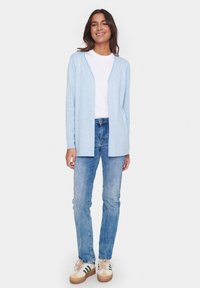 Ljusblå cardigan med öppen framsida, mjuk textur. Kombinerad med vit t-shirt och bleka blå jeans, med en avslappnad silhuett och låga skor.
