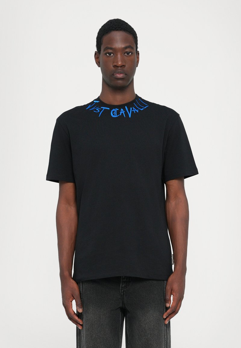 Svart bomullströja med blå broderad text runt halsringningen, design med rund hals och korta ärmar. Texten säger "Just Cavalli."