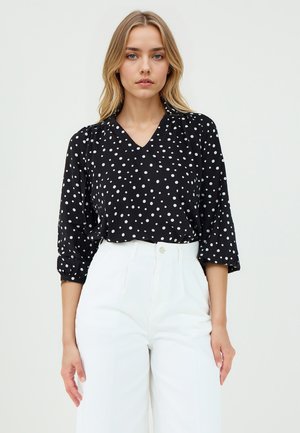 Blusa nera con pois bianchi, scollo a V e maniche a tre quarti, abbinata a pantaloni bianchi a vita alta e gamba larga. Tessuto dalla texture liscia.