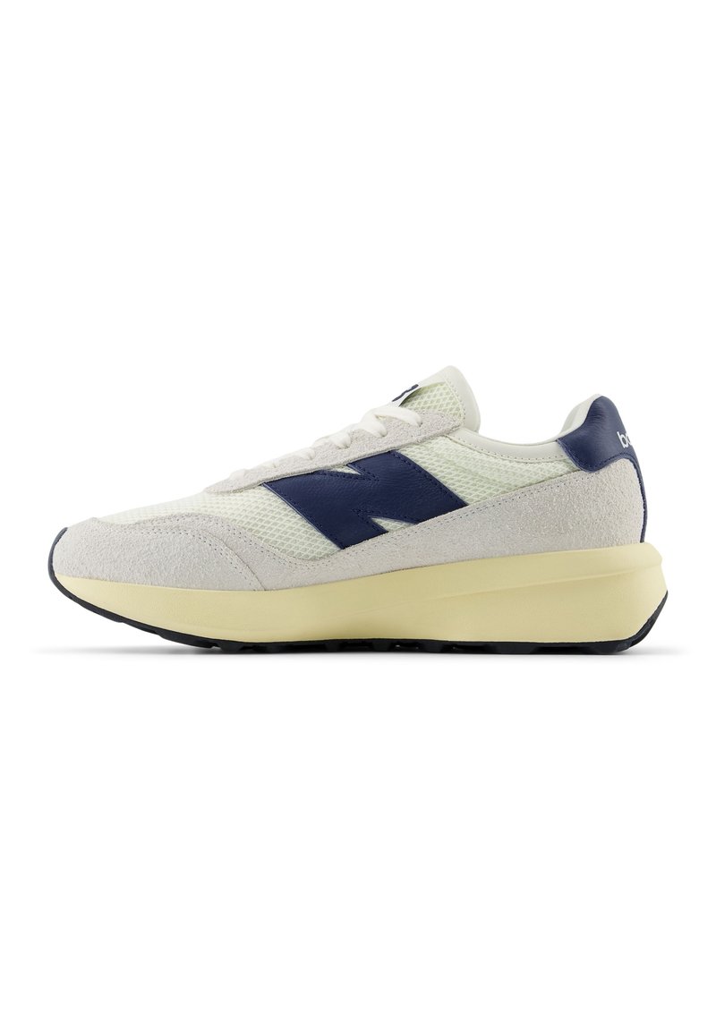 White and navy athletic shoe featuring mesh and suede materials, rounded toe, lace-up design, and a cushioned cream sole.