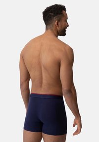 Boxers azul marino con una cinturilla roja, hechos de tela suave, con un diseño ajustado y sin patrones ni accesorios adicionales.