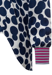 Blusa realizzata in tessuto bianco con grandi pois blu navy e polsini a righe nei colori blu navy, rosa e bianco. Texture morbida e vestibilità ampia.