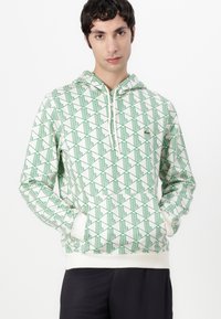 Felpa con cappuccio in crema chiaro con motivo geometrico verde, polsini a costine e tasca frontale. Realizzata in morbido tessuto misto cotone.
