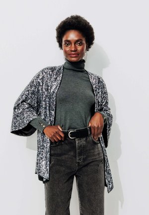 Un kimono à motifs noir et blanc sur un col roulé gris, associé à un jean en denim taille haute. Il présente des manches larges et une ceinture.