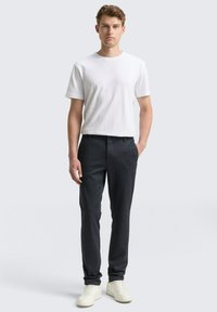 Wit T-shirt met korte mouwen gecombineerd met donkergepatteerde broek en witte sneakers. De outfit heeft een losse pasvorm en een klassiek ontwerp.