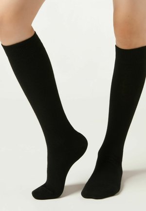 Calze nere alte fino al ginocchio realizzate in tessuto liscio, con un design aderente, polsini a coste e punta senza cuciture per un comfort migliorato.