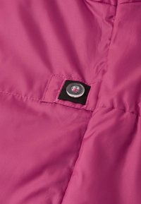 Růžová polstrovaná textilie s lesklým povrchem, se zaobleným průhledným knoflíkem a černým textilním akcentem, kde je knoflík připevněn.