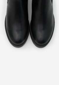 Pár černých kožených kotníkových bot s kulatými špičkami a nízk�ými podpatky, vyfocených shora na bílém pozadí.