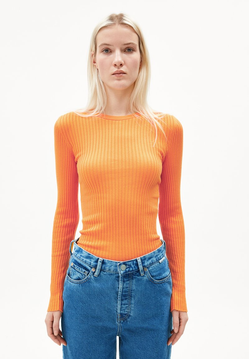 Rippenshirt mit langen Ärmeln in leuchtendem Orange, kombiniert mit hoch geschnittenen blauen Denim-Jeans im klassischen Fünf-Taschen-Stil und heller Waschung.