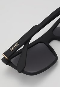 Ochelari de soare negri cu finisaj mat, formă pătrată, lentile întunecate și logo accentuat cu aur pe brățară. Hinge durabil cu design elegant.