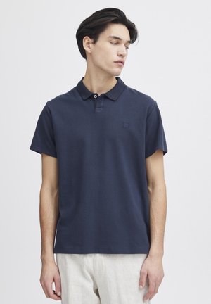 Marineblå polo skjorte laget av bomull, med klassisk krage, korte ermer og subtilt logo på brystet. Enkel design, avslappet passform.