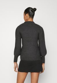 Dark gray ribbed knit sweater with a high collar, puffed sleeves, and side seam detail, displayed from the back. Accentuates textured fabric.