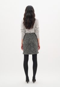 Pull gris, jupe vichy noir et blanc, portée avec des collants noirs et des talons. La tenue présente un design ajusté et un tissu texturé.