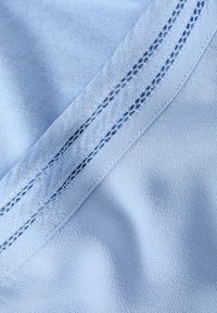 Un tessuto azzurro chiaro con una superficie liscia e sottile presenta un punto decorativo lungo il bordo, creando un aspetto stratificato.