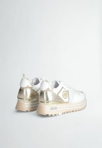 Zapatillas deportivas blancas con acentos metálicos en dorado, paneles texturizados y suelas de goma. Presentan detalles de logotipo y un diseño de cierre con cordones.