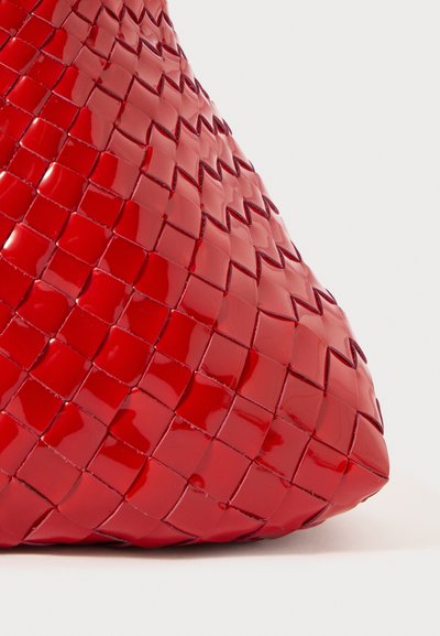 Červená tkaná kabelka s lesklou, prošívanou texturou a zaobleným dnem. Obsahuje jedinečný propletený design, který ukazuje ostré a čisté linie.