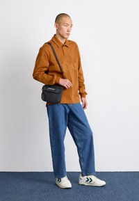 Brown long-sleeve polo shirt with a collar, blue loose-fit jeans, white sneakers with green accents, and a black crossbody bag.