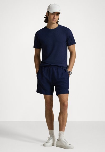 Ναυτικό αθλητικό t-shirt με κοντά μανίκια, συνδυασμένο με αντίστοιχες βερμούδες και λευκά αθλητικά παπούτσια. Διαθέτει χαλαρή εφαρμογή και ελαστική μέση.