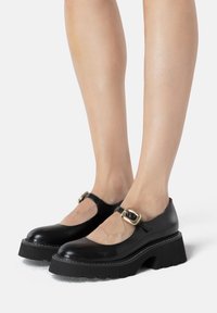 Czarne skórzane buty Mary Jane z zaokrąglonym noskiem, zapięciem na kostkę z złotą klamrą oraz grubą, teksturowaną czarną podeszwą.