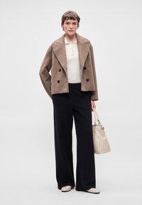 Brūna divrindas vilnas jaka, balts ribots topiņš, tumši plati svītraini bikses un gaiša rokassoma. Apavi: gaišas krāsas dzīvokļi.