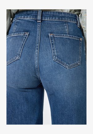 Jeans in denim blu a vita alta con tasche posteriori, cuciture a contrasto e una texture liscia, mostrati da dietro.