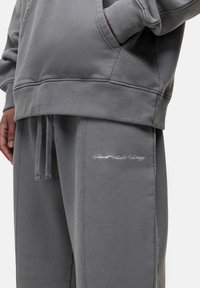 Grijze hoodie en joggers van zachte stof, met een kangoeroezak en geborduurde tekst op de joggers. Comfortabele, relaxed fit.